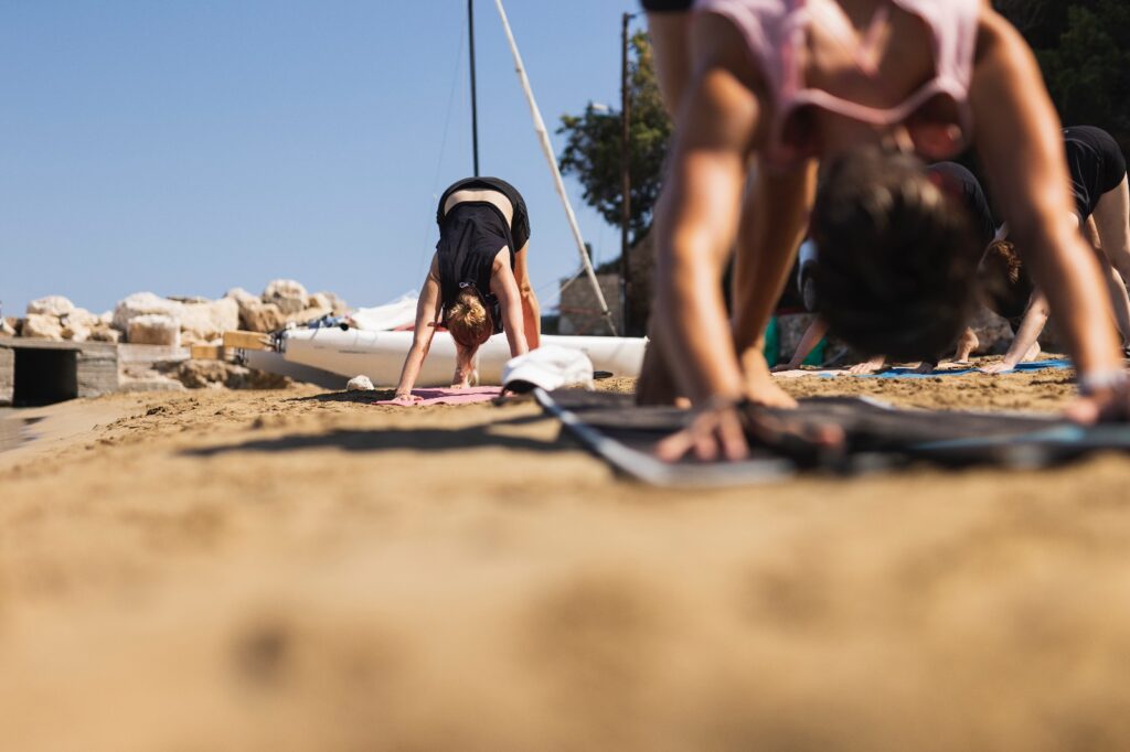Photographie d'un groupe de personnes pratiquant un chien tête en bas pendant un cours de yoga à la plage